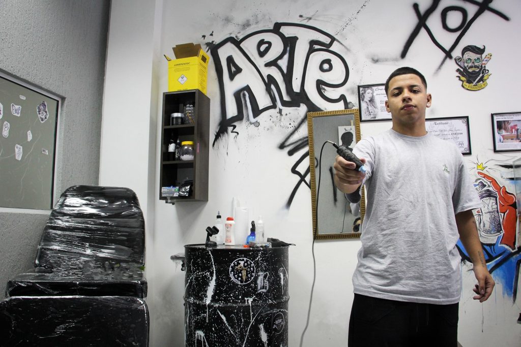 Tatuador usando a pomada TKTX para tatuadores, segurando uma máquina de tatuagem e tirando uma foto em seu estúdio.